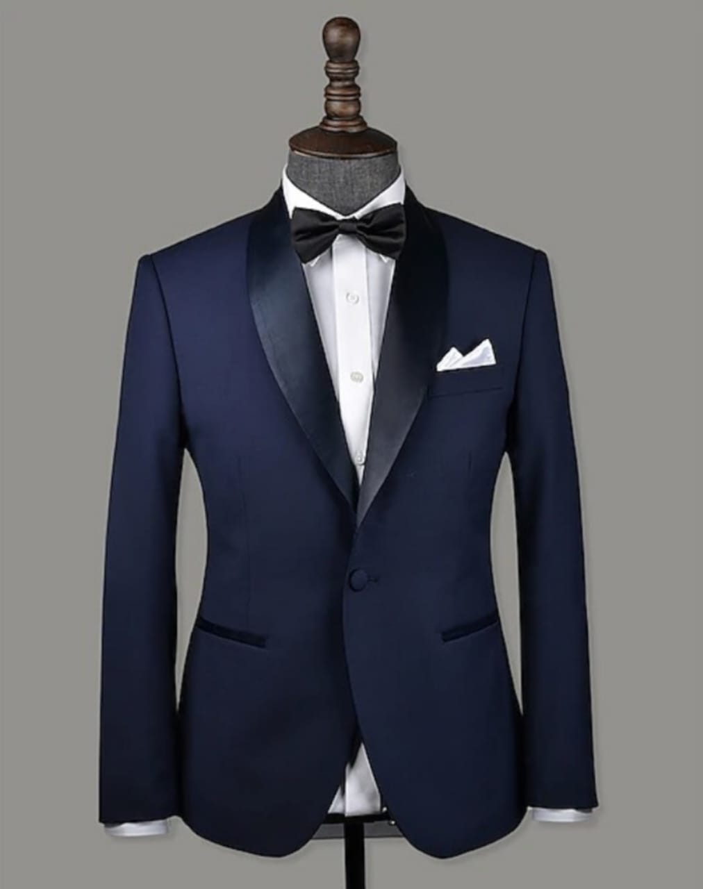Best wedding suits for groom – Elegant navy blue tuxedo with a black satin shawl lapel, paired with a crisp white shirt, black bow tie, and a white pocket square, perfect for a sophisticated wedding look.