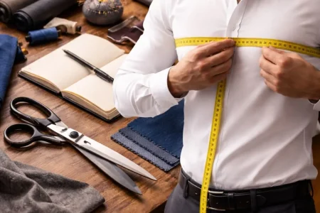 Man using a measuring tape to learn How to Measure Yourself for a Suit at Home accurately in front of a mirror.